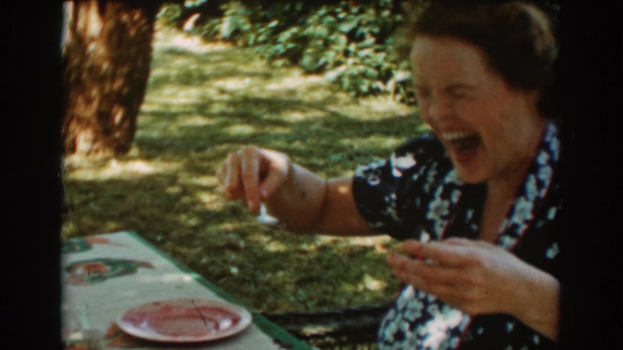 Woman laughing while holding a spoon beside a plate outdoors.