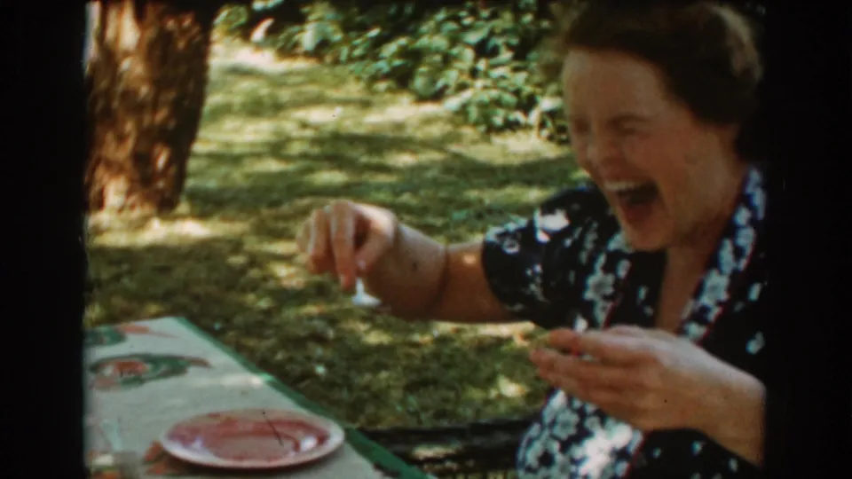 The woman laughs broadly beside a pink plate at an outdoor picnic table in the Auburn, California garden scene.