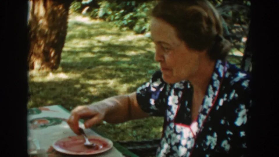 The woman looks down and uses a spoon on the plate during the 1939 Auburn garden picnic footage.