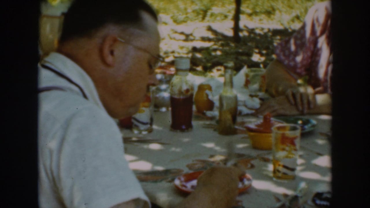 A 1939 Auburn outdoor meal view shows the man in profile at a table set with drinks, condiments, plates, and food.