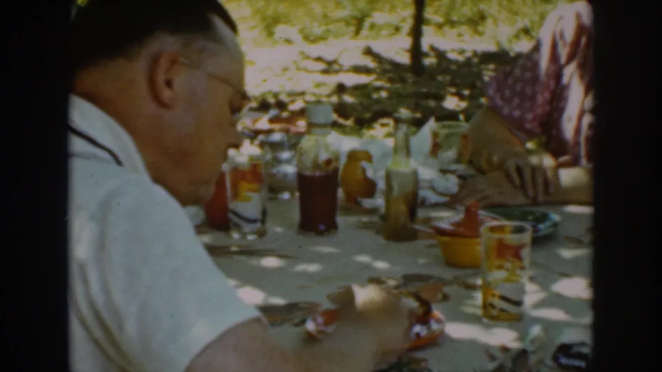 The home-movie frame shows a man at an outdoor meal in Auburn, California, surrounded by glasses, condiments, and plates.