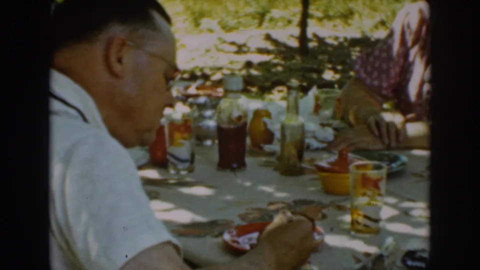 A man in suspenders sits at a shaded Auburn, California table in 1939, with drinks, condiments, food, and another adult partly visible.
