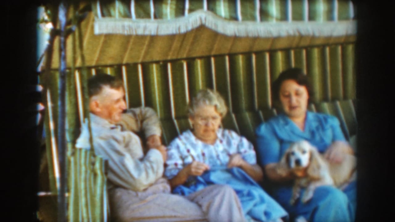 Three adults sit on a striped outdoor seat while one woman holds a small dog and another knits.