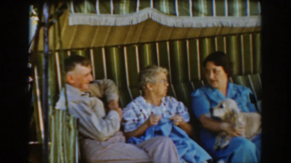 The adults remain seated on a striped chair or swing in Auburn, California, with the center woman turning toward the dog held by the woman in blue.