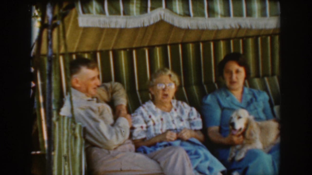 Three adults sit close together in a cabana as the dog faces forward from the younger woman's lap.