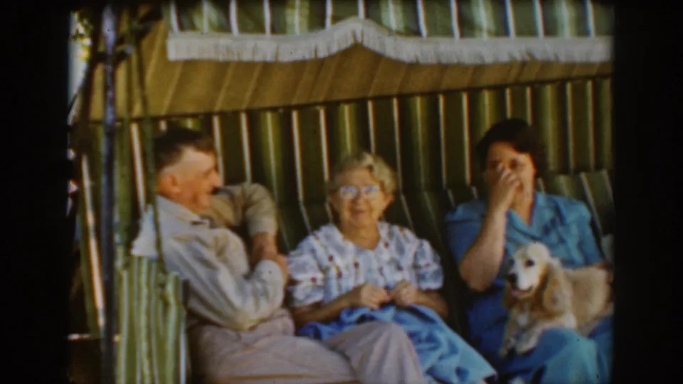 Auburn, California, 1939 home-movie frame showing a laughing family moment in a striped cabana, with knitting visible in the elderly woman's hands.