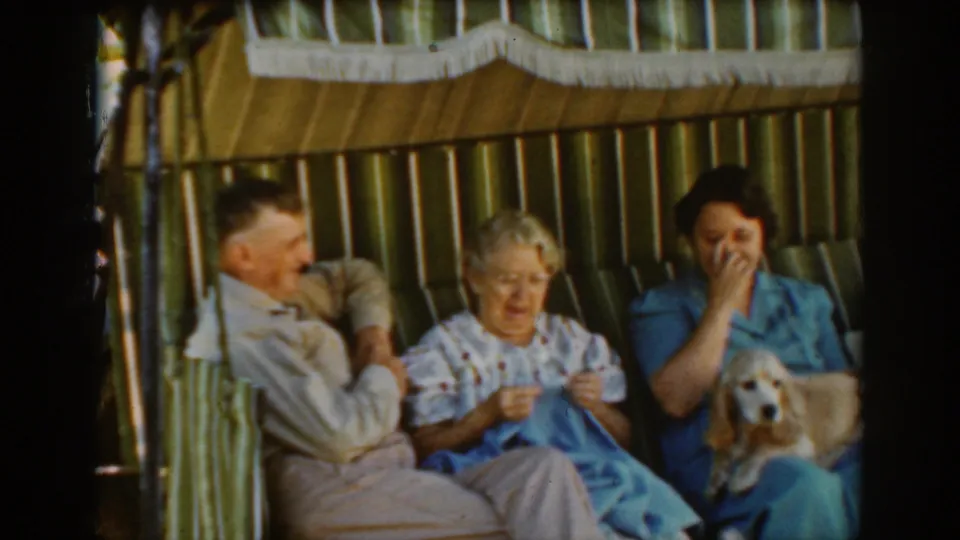 Auburn, California, 1939 frame showing three seated adults sharing a relaxed moment in a striped cabana with a small dog nearby.