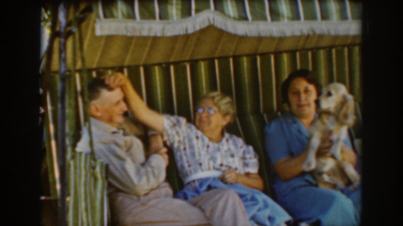 Three adults sit on a striped porch swing while an older woman reaches toward a man.