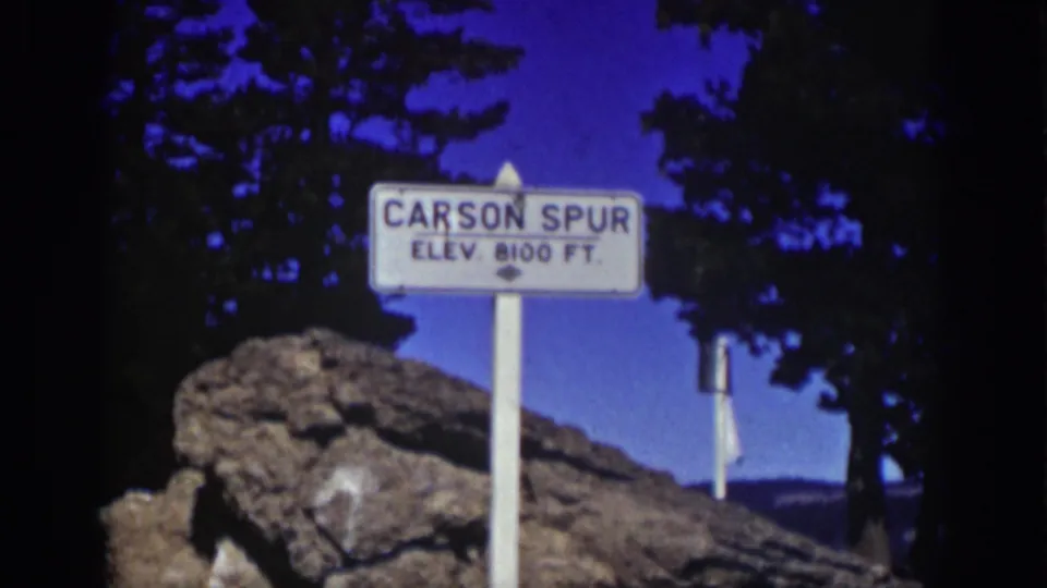 1939 Lake Tahoe-area frame showing a white Carson Spur elevation 8100 feet sign against rocks, pines, and blue sky.