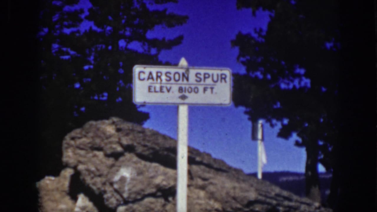 Carson Spur sign framed by pine silhouettes and roadside rocks.
