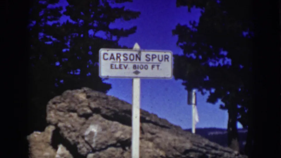 White Carson Spur elevation sign in a Lake Tahoe-area mountain setting, with pine shadows, rocks, and a deep blue sky.