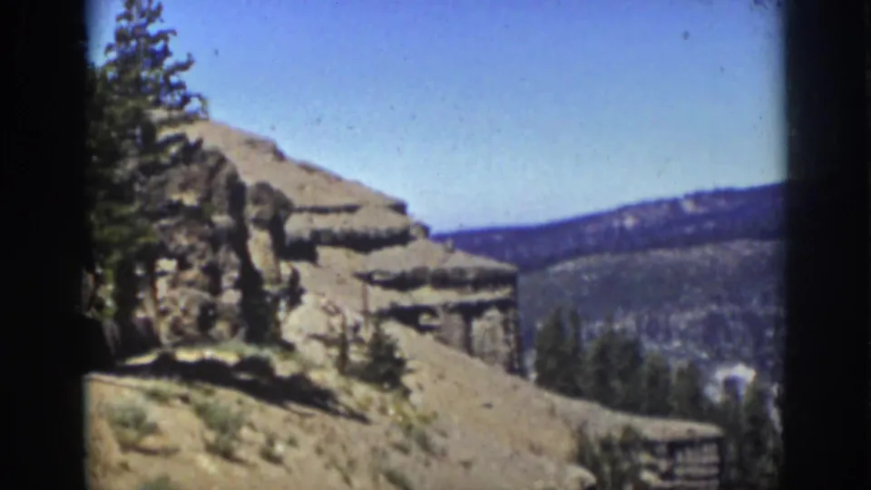 1939 Lake Tahoe-area view across a rocky slope, scattered pines, pale terrain, and distant forested ridges under blue sky.