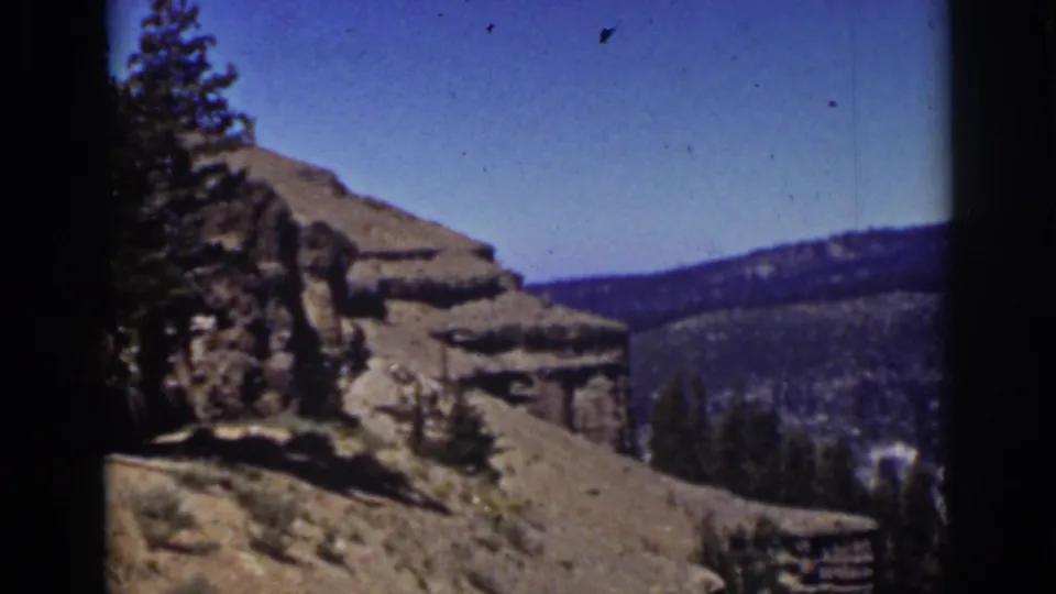 Lake Tahoe-area mountain view with layered rocks, a pine at frame edge, distant wooded hills, and visible 8mm film grain.