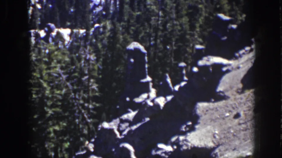 Vintage 8mm Lake Tahoe view of clustered rocks, dense pine growth, and a small dirt clearing with dark frame edges.