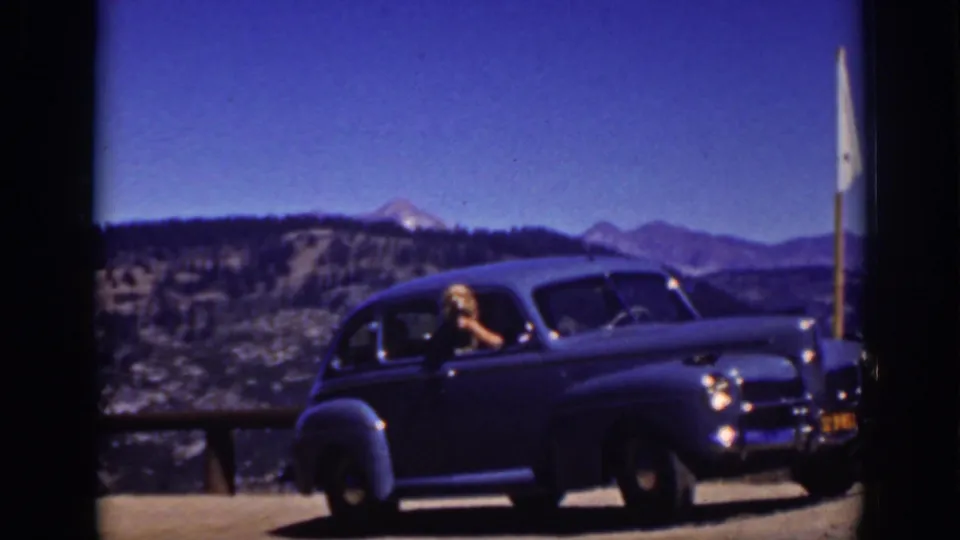 1939 Lake Tahoe home-movie frame showing a blue sedan at a scenic overlook, with a blonde woman leaning from the driver's window.