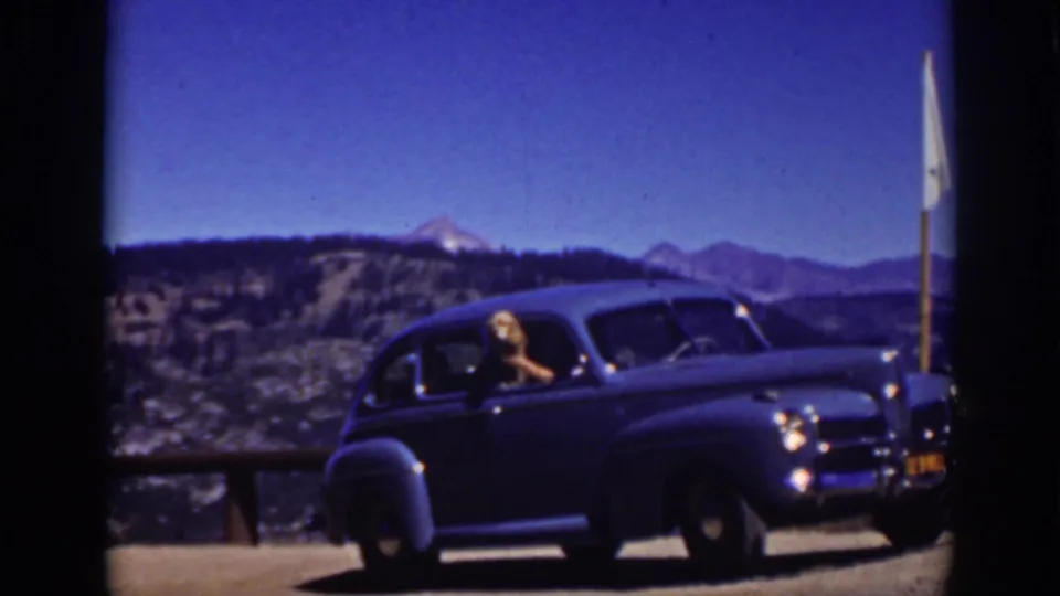 Lake Tahoe, 1939, with a blue vintage sedan in sunlight, a woman at the driver's window, and mountain scenery in the background.