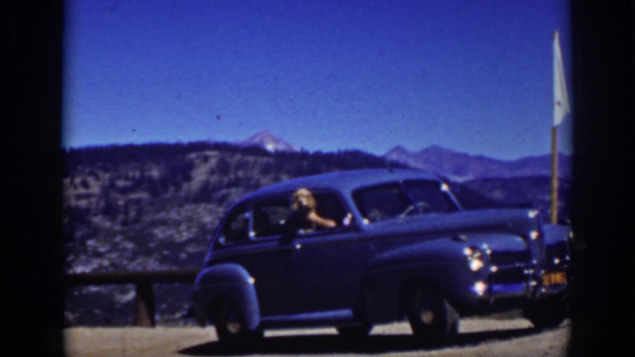 Vintage blue car at a mountain overlook with a woman leaning from the window.