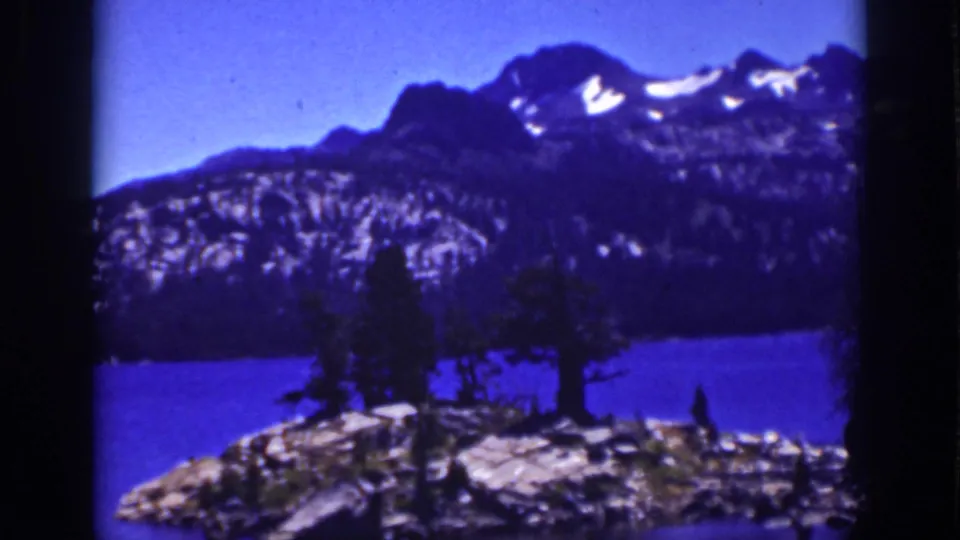Lake Tahoe 8mm view of a rocky, tree-lined lakeshore with blue water and snow-patched mountain ridges beyond.