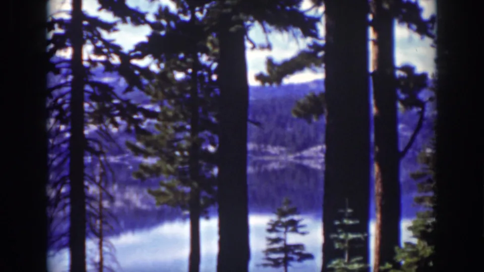 Final 1939 Lake Tahoe frame showing a still scenic view through pines toward water, forested shore, and mountains.