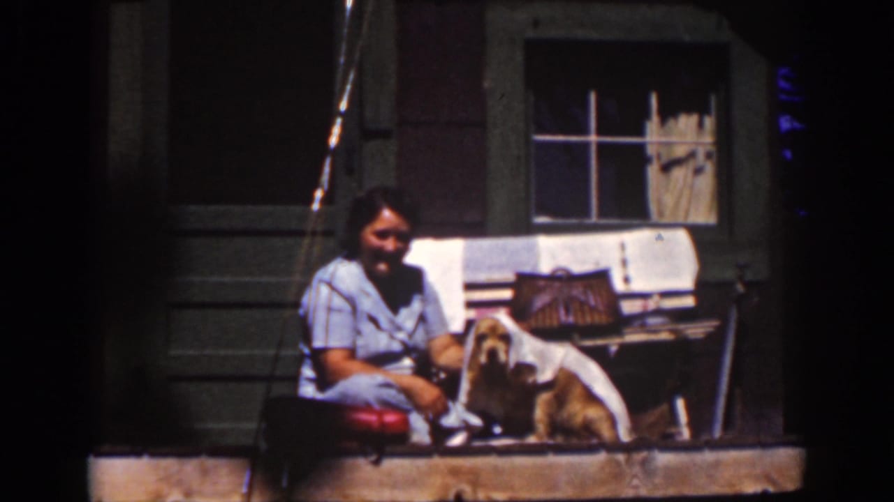 Woman sits on a cabin porch beside a small dog and cloth.