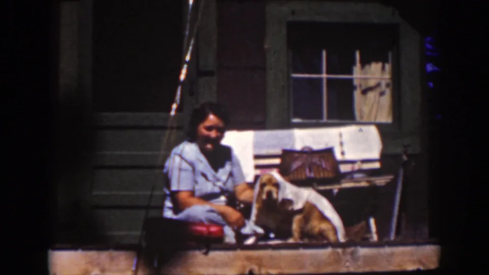 At Lake Tahoe in 1939, a woman sits on a wooden cabin porch with a small dog, cloth, bench, and curtained window visible.