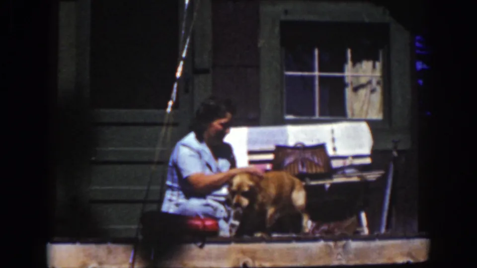 1939 Lake Tahoe home-movie frame showing a woman seated on a porch step washing or tending a golden-colored dog.