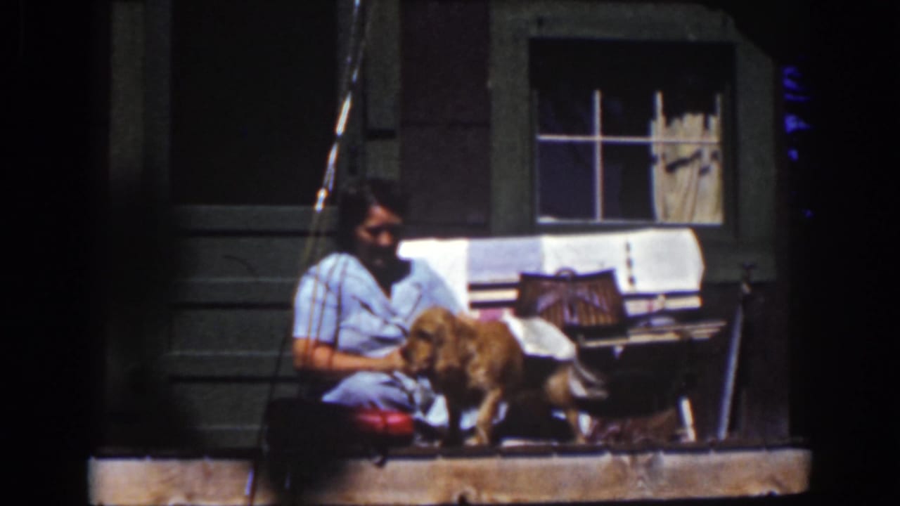 A woman on a Lake Tahoe porch holds a white towel as a golden dog stands close to her in the 1939 home-movie frame.