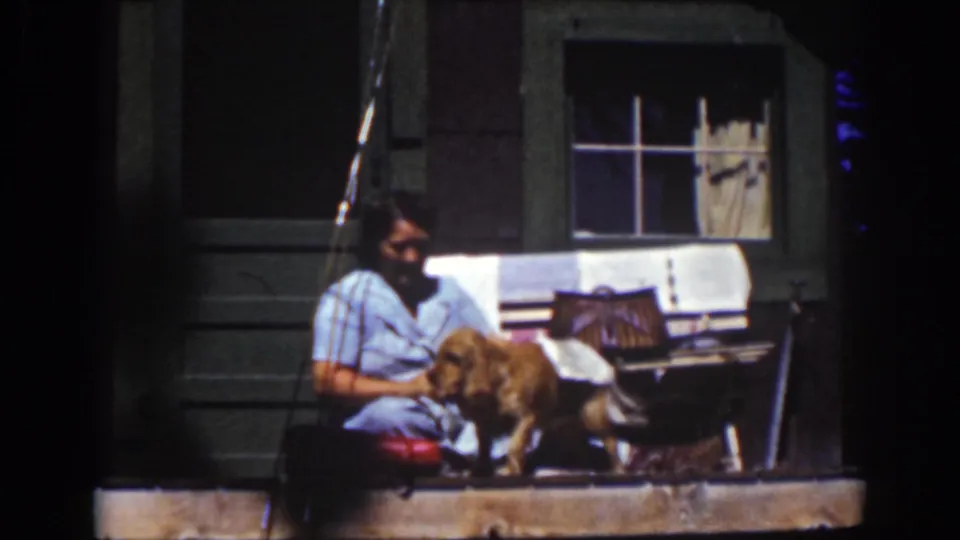 A woman on a Lake Tahoe porch holds a white towel as a golden dog stands close to her in the 1939 home-movie frame.