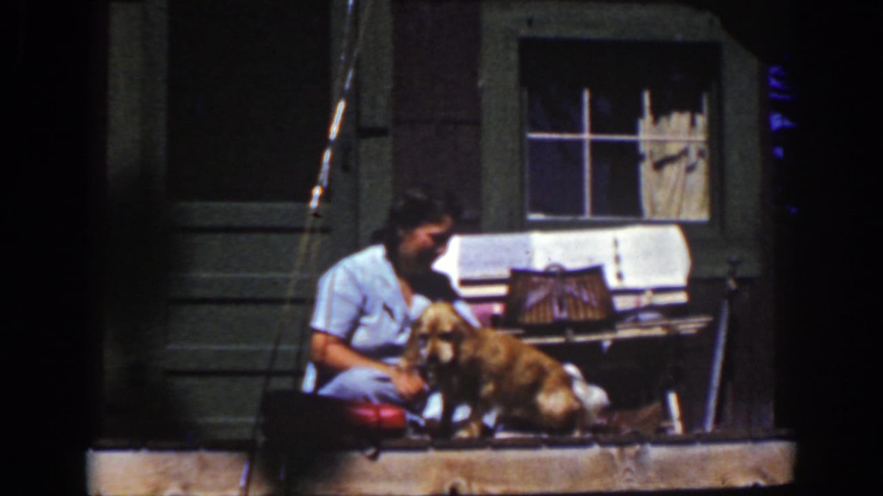 A woman in a light blue dress sits beside a golden dog on a Lake Tahoe porch in this 1939 8mm home-movie still.