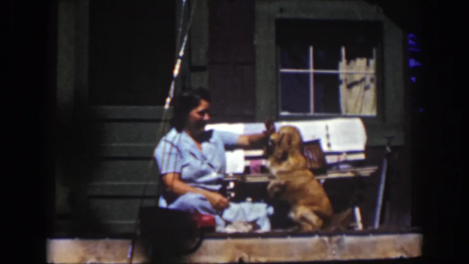 A woman seated on a rustic Lake Tahoe porch rests near a golden dog, with cabin siding and a curtained window behind them.