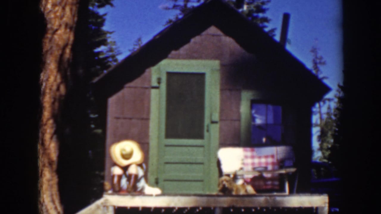 Person in a straw hat seated on a small cabin porch beside a green door.