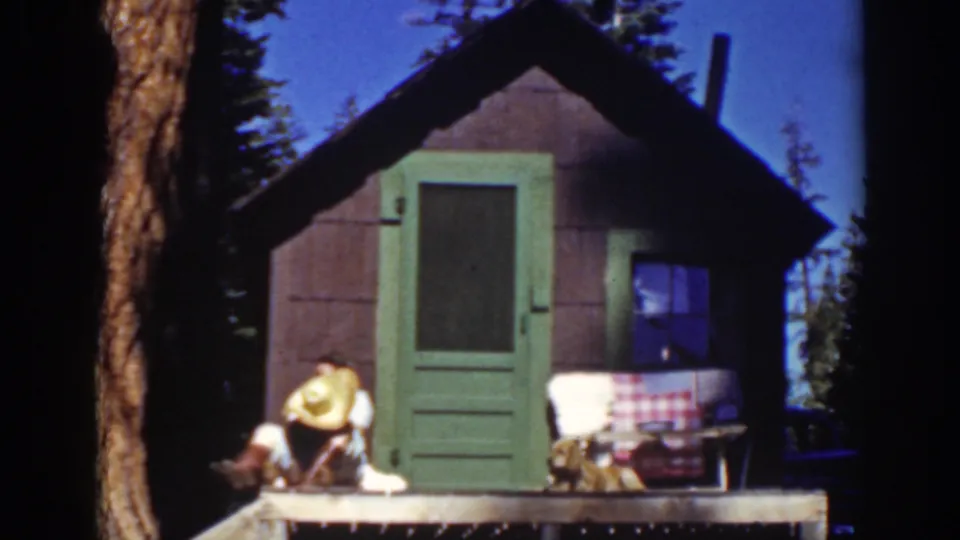 Lake Tahoe 1939 home-movie frame of a person leaning forward on a small cabin porch under pine trees.