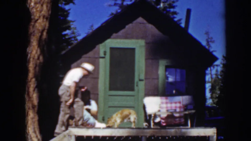 The man leans down toward the seated woman on the porch of the small Lake Tahoe cabin as the dog stands nearby.