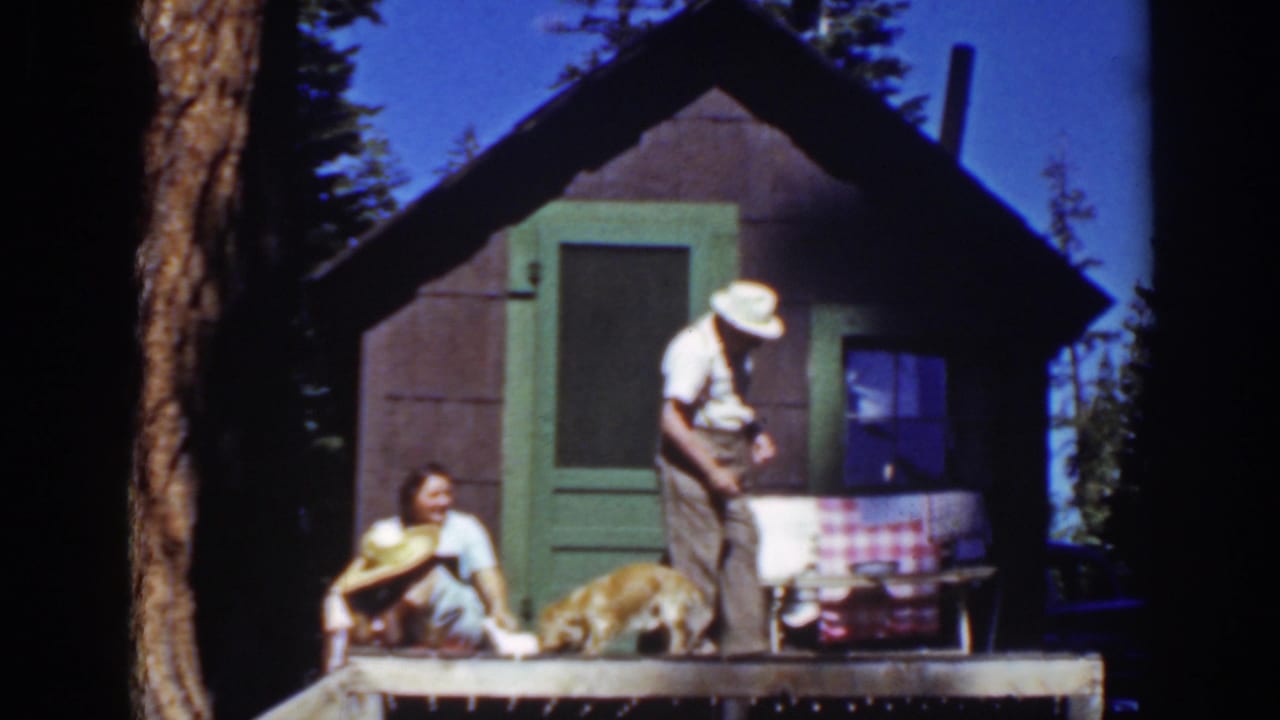 Couple on a cabin porch with a dog and straw hat.