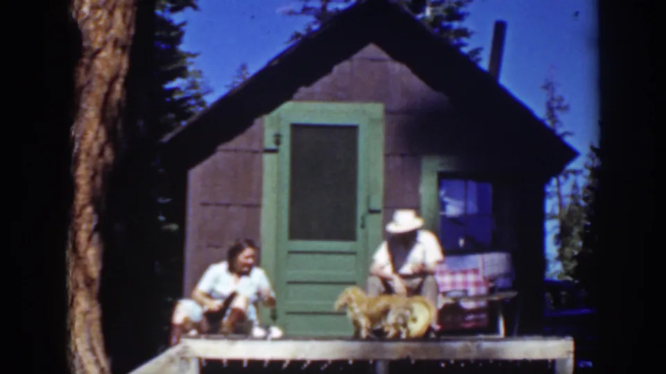 The final frame holds on the Lake Tahoe cabin porch as the couple and dog gather near the green door and small window.
