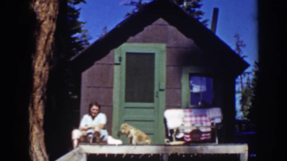 Lake Tahoe 1939 cabin-porch frame with a seated woman and dog near the right side of the small structure.