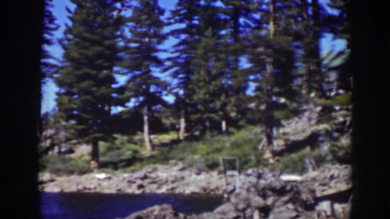 Pine-covered rocky shoreline with part of a cabin visible above the lake.