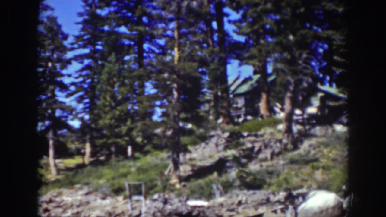 Rocky hillside with pine trees and a cabin roof visible near the upper right.