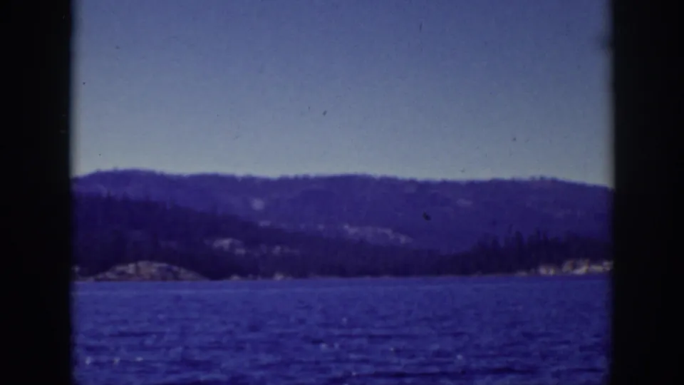 1939 Lake Tahoe frame looking across blue water toward dark wooded hills and a pale clear sky.
