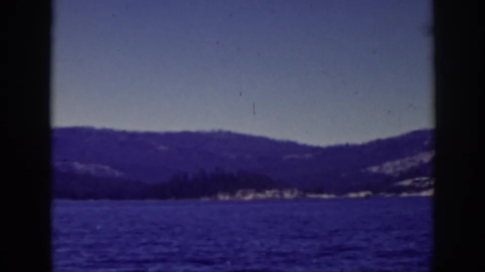 Final 1939 Lake Tahoe frame showing blue water in the foreground and a dark tree-lined shoreline below distant hills.
