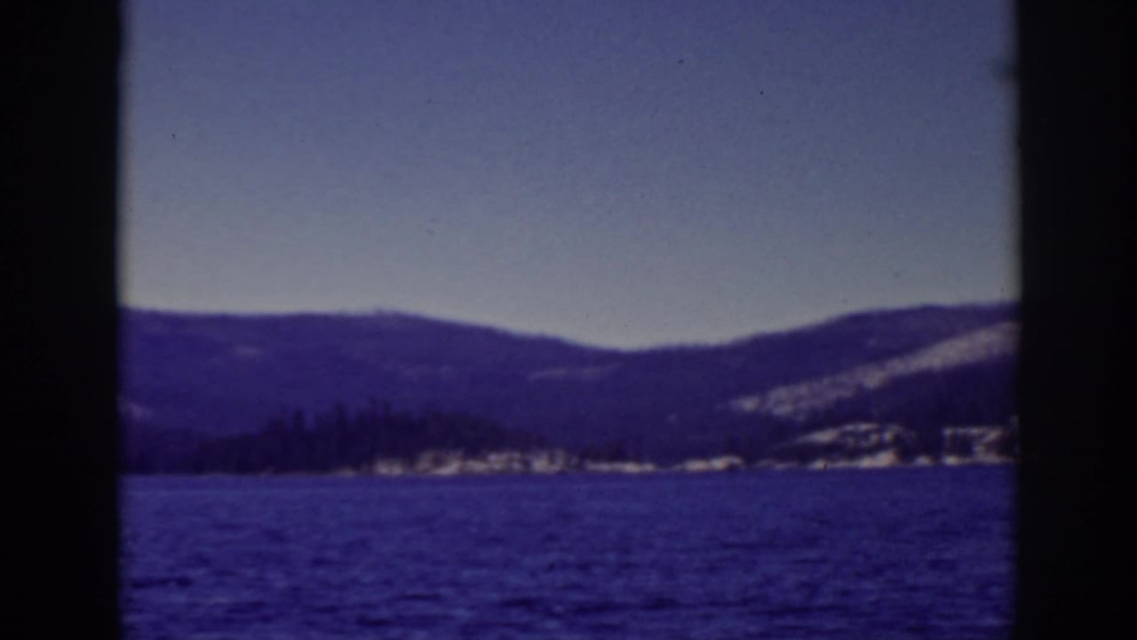 Blue lake with snowy mountains in the distance, framed by dark 8mm film borders.