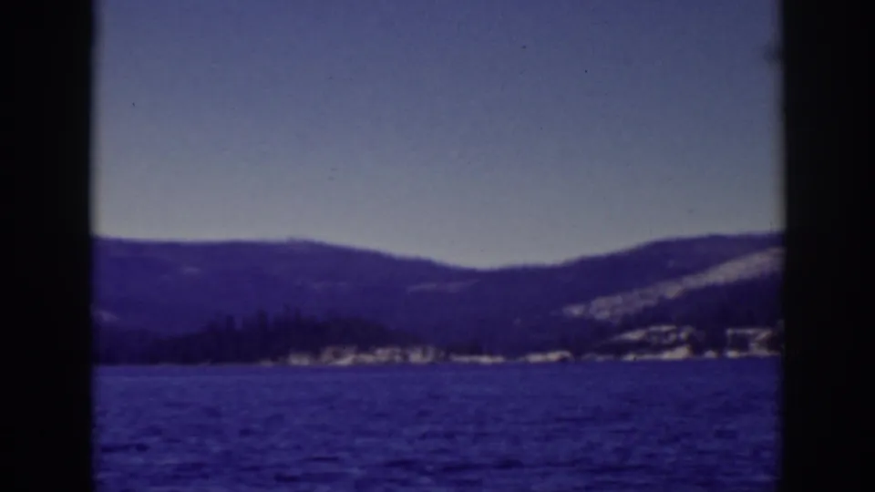 1939 Lake Tahoe home-movie frame showing open water, a distant snowy mountain ridge, clear sky, and heavy dark film borders.