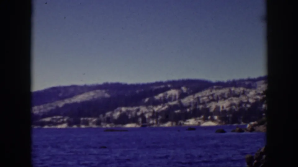 Lake Tahoe winter view from 1939 home-movie footage, showing dark lake water, snowy distant slopes, shoreline, and edge artifacts from the 8mm frame.