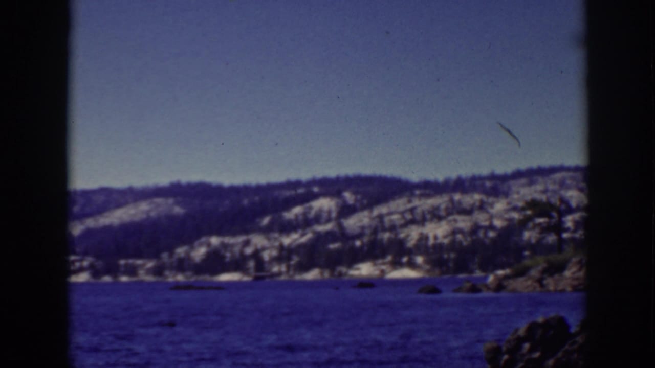 Lake water with distant snow-dusted hills and rocky shoreline seen through dark 8mm frame edges.
