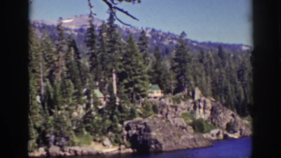 1939 Lake Tahoe home-movie view of cabins among evergreens on a rocky shoreline with blue lake water below.