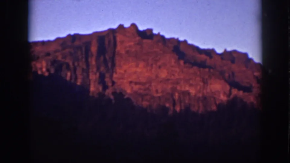 Lake Tahoe 1939 home-movie frame with a warm red mountain ridge, blue sky, and deep shadow below.