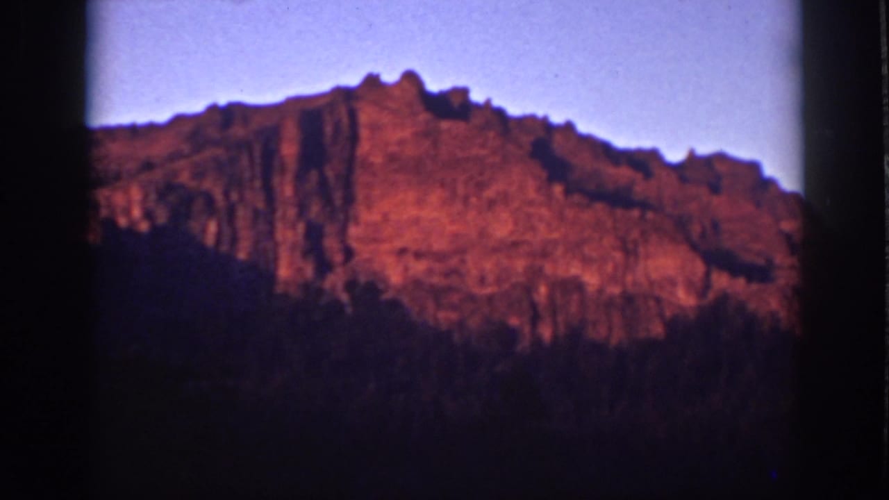 Red-lit rocky ridge above a dark foreground under a pale twilight sky.
