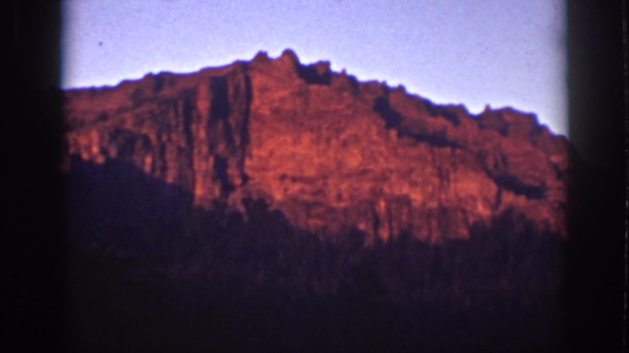 Red morning light on rocky cliffs above dark tree silhouettes.