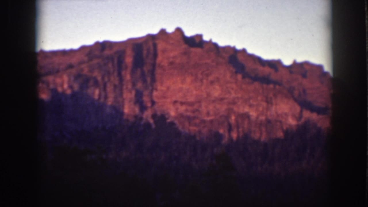 Reddish mountain rock face above a dark forest under a pale sky.