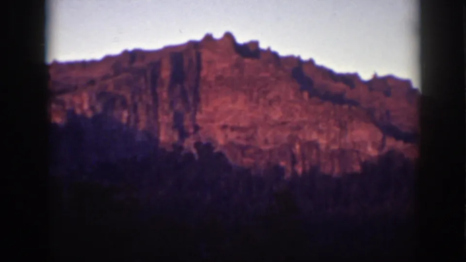 1939 Lake Tahoe 8mm frame showing the cliff face in warm light, with a dark wooded slope across the foreground.